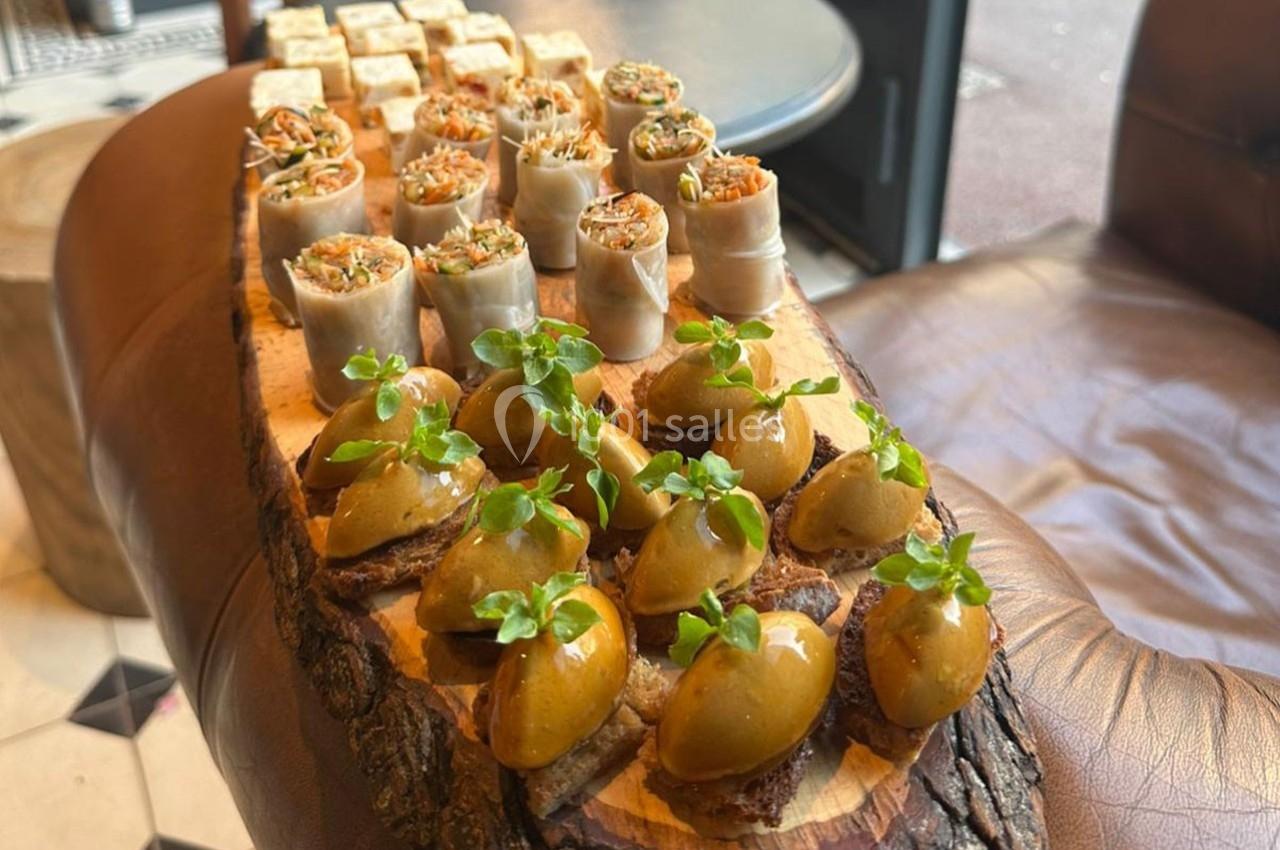 Assortiment de bouchées apéritives disposées sur une planche en bois, comprenant olives garnies et rouleaux farcis.