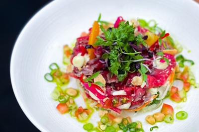 Dessert raffiné présenté dans un bol noir, décoré de fruits rouges, de crème blanche et de touches végétales.
