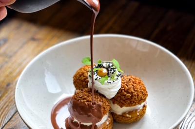 Dessert raffiné présenté dans un bol noir, décoré de fruits rouges, de crème blanche et de touches végétales.
