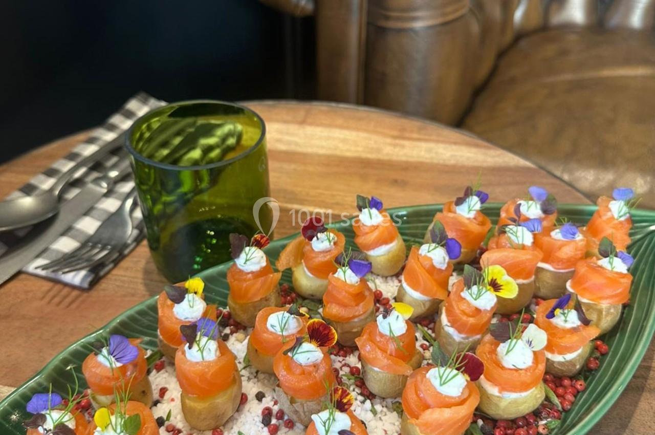 Plateau de bouchées apéritives au saumon fumé, décorées de fleurs comestibles, sur un lit de sel et de baies rouges.
