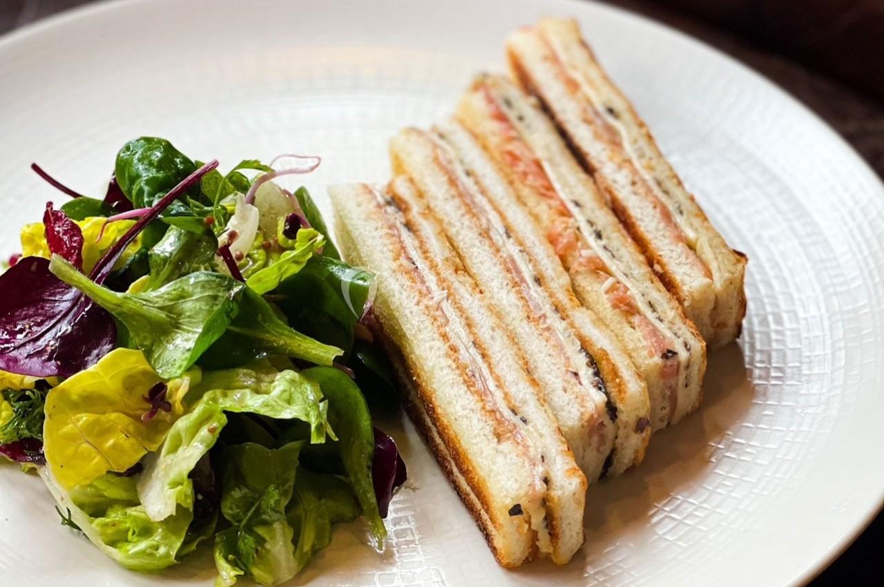 Assiette contenant un sandwich club tranché accompagné d'une salade verte variée.