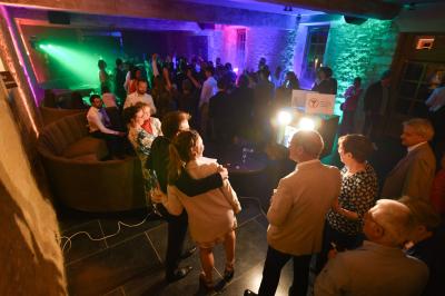 Des personnes dansent et discutent dans une salle éclairée par des lumières colorées lors d'un événement festif.