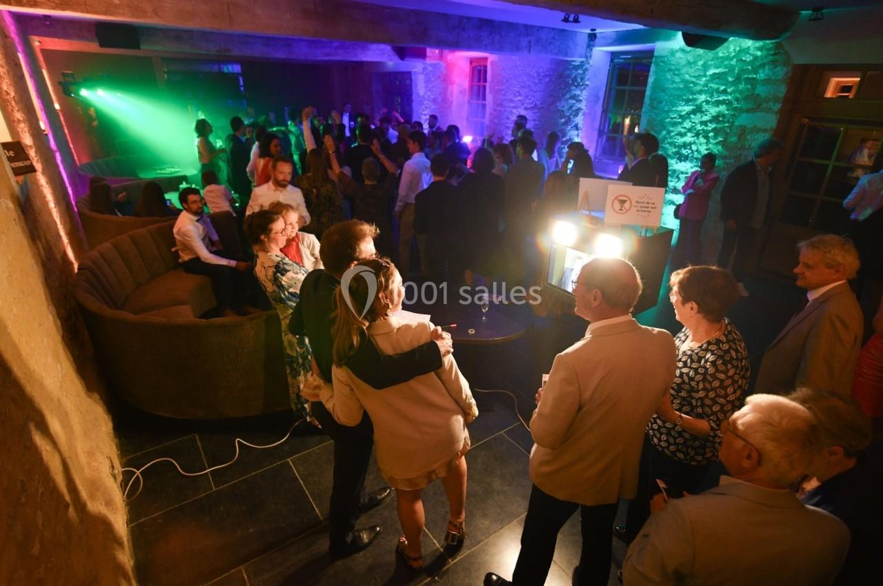 Des personnes dansent et discutent dans une salle éclairée par des lumières colorées lors d'un événement festif.