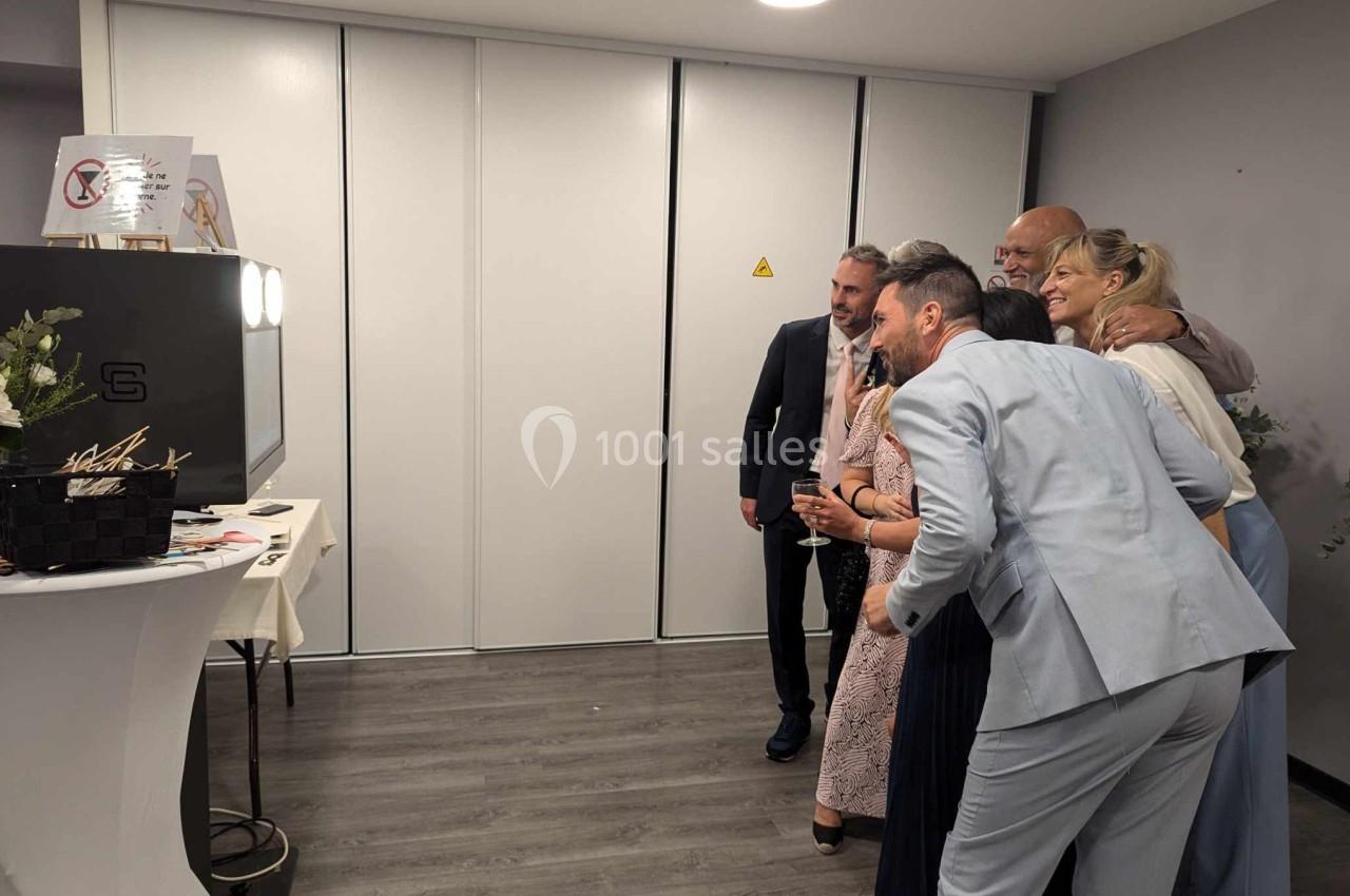 Des personnes posent ensemble devant une borne photo dans une salle au sol en parquet et murs clairs.