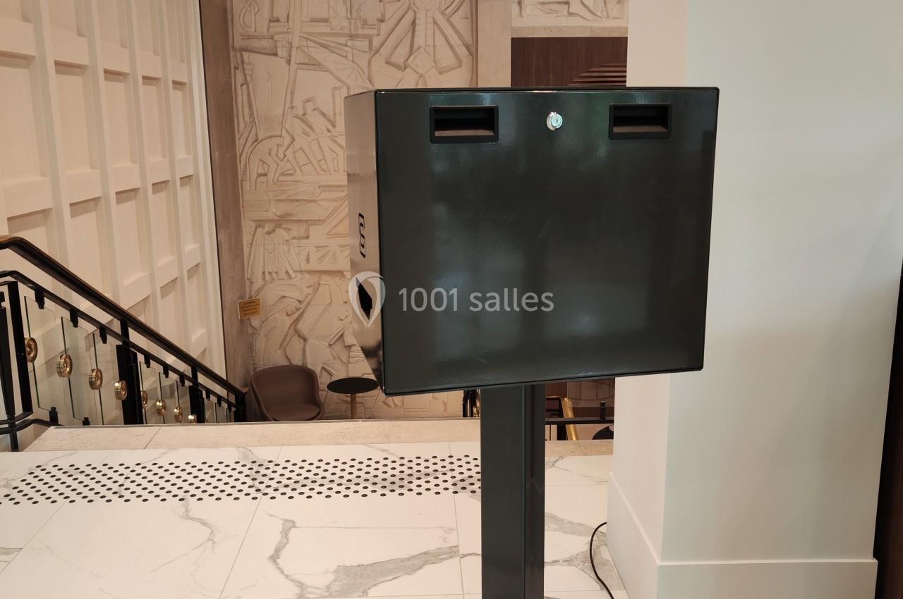 Borne noire sur pied dans un espace intérieur moderne avec sol en marbre et mur décoratif en arrière-plan.