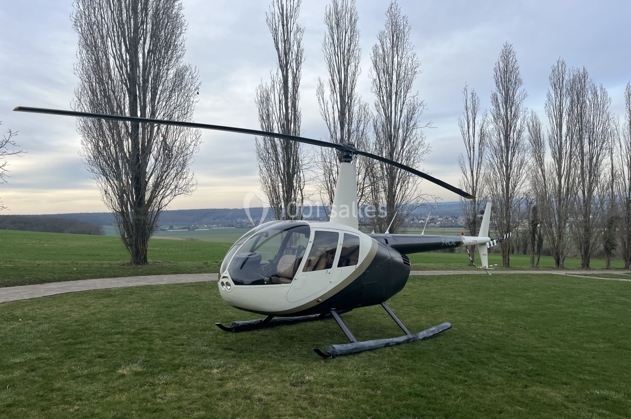 Hélicoptère posé sur une pelouse verte, avec des arbres et un paysage vallonné en arrière-plan.