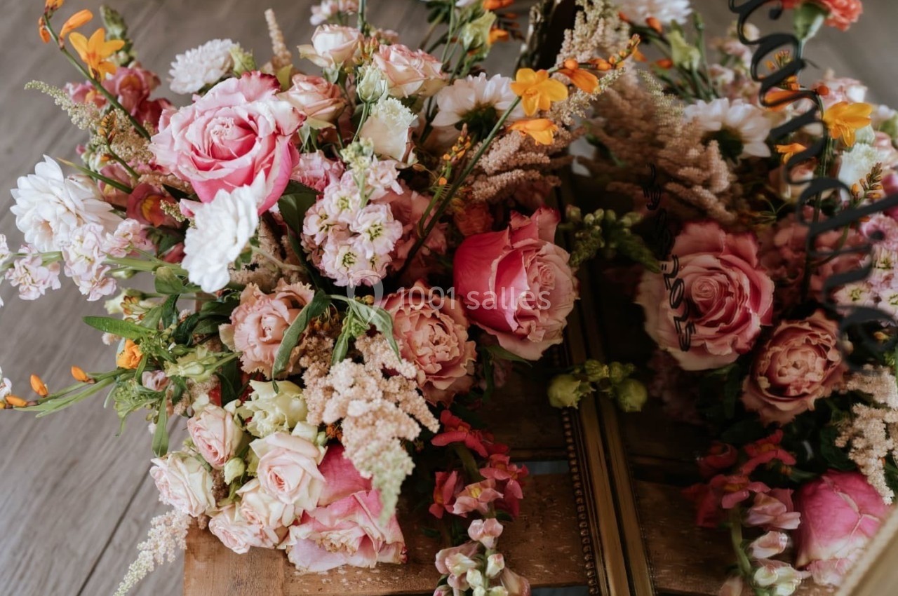 Bouquet de fleurs variées aux tons roses, blancs et orangés, posé sur une surface en bois avec un miroir reflétant l…