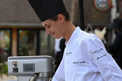 Un chef pâtissier en toque décore une tarte meringuée à l'extérieur, près d'un batteur sur socle.