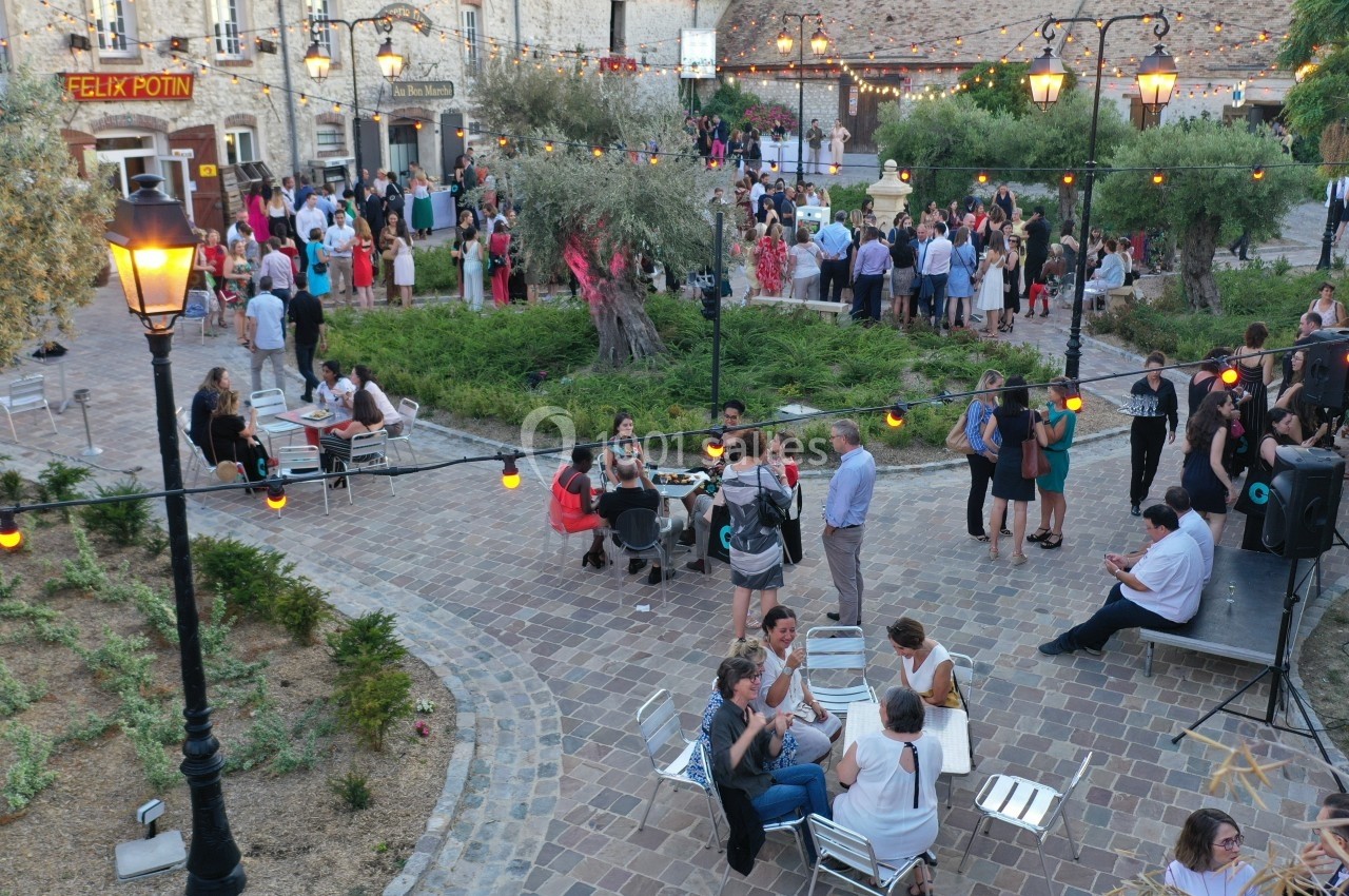 Groupe de personnes réunies dans une cour pavée avec des guirlandes lumineuses et des arbres autour.