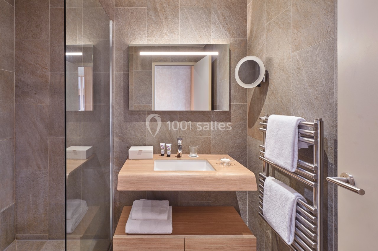 Salle de bain moderne avec lavabo en bois, miroir éclairé, douche vitrée et porte-serviettes avec serviettes blanches.