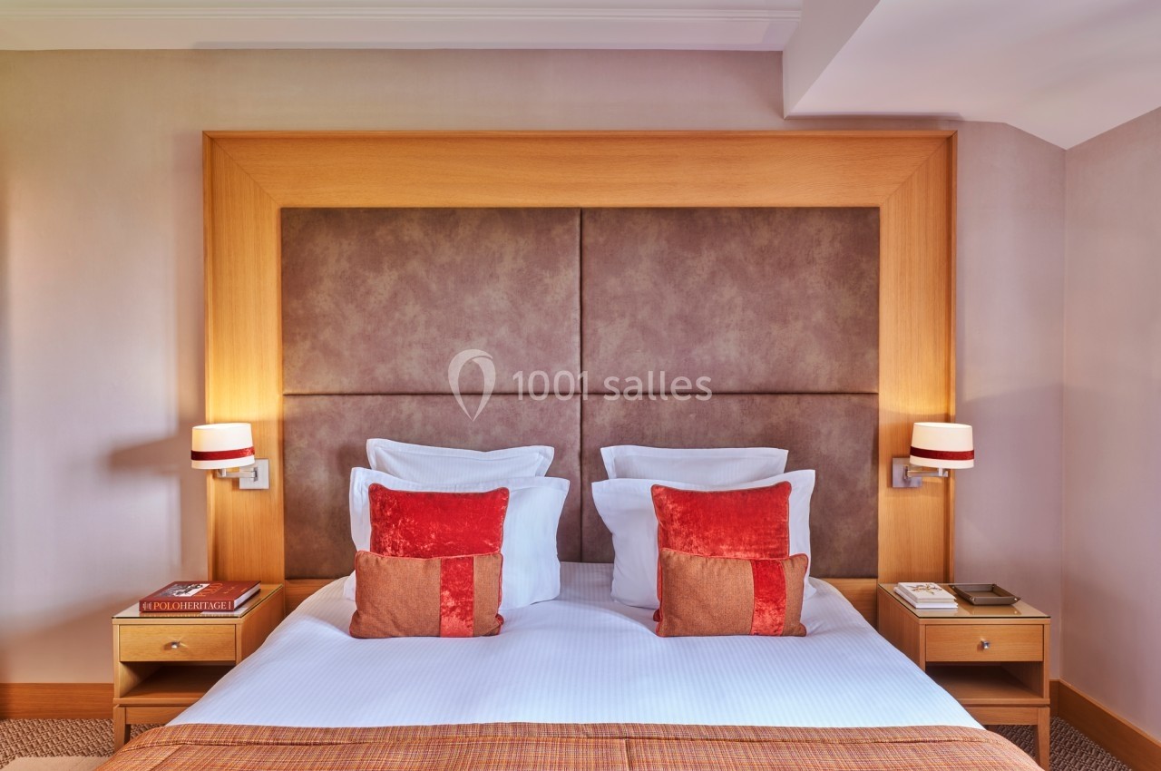 Lit double avec tête de lit en bois, coussins rouges, lampes murales et tables de chevet avec livres.