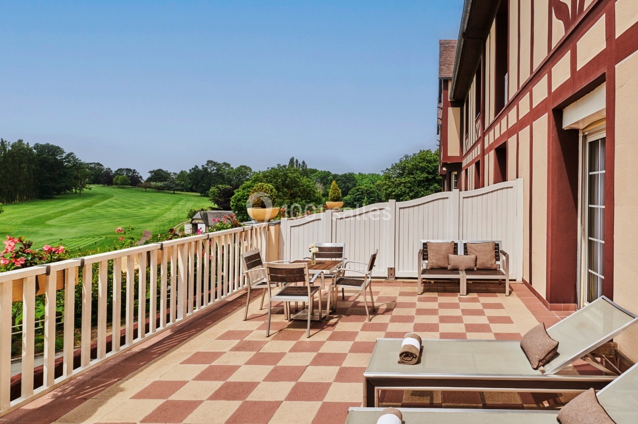 Terrasse avec mobilier de jardin, chaises longues et vue sur un terrain de golf entouré de verdure.