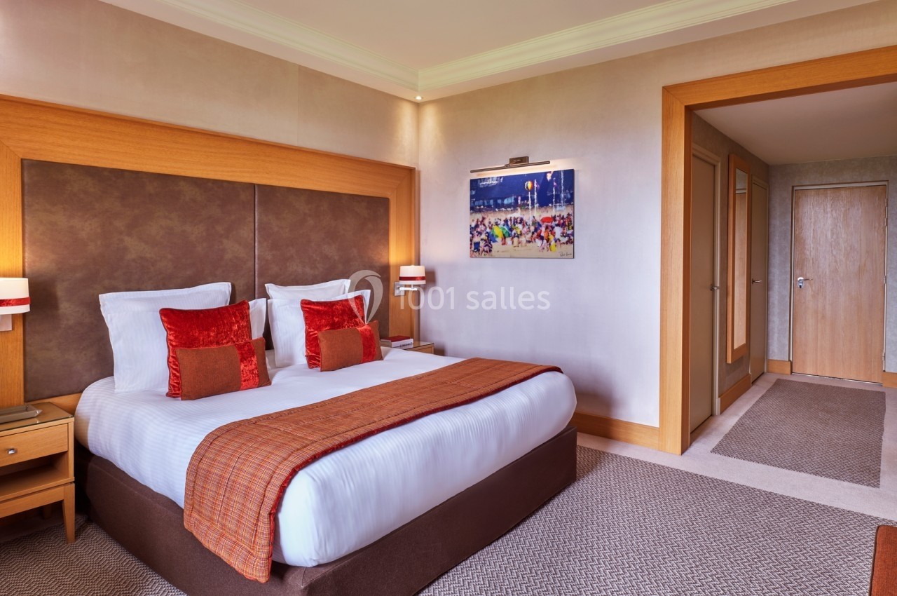 Chambre d'hôtel avec un grand lit double, des oreillers rouges, un éclairage doux et une décoration murale colorée.