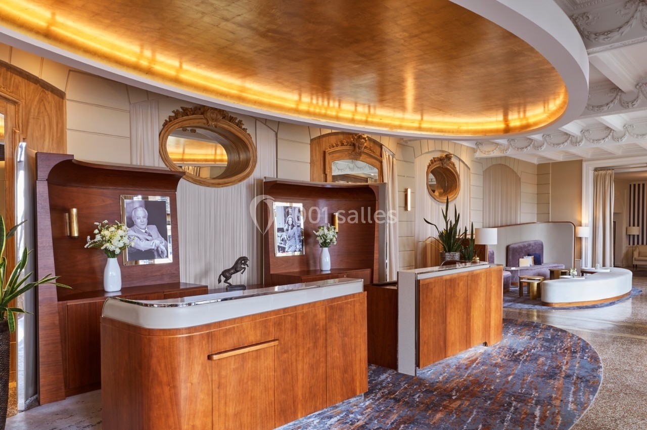 Comptoirs en bois avec décorations élégantes dans un hall d'hôtel au plafond doré et mobilier raffiné.