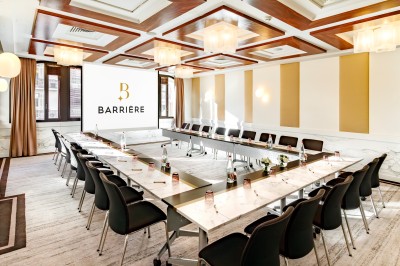 Transats avec coussins rouges alignés sur un ponton en bois, face à la mer, avec parasols blancs et vue sur un phare.