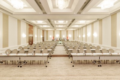 Transats avec coussins rouges alignés sur un ponton en bois, face à la mer, avec parasols blancs et vue sur un phare.