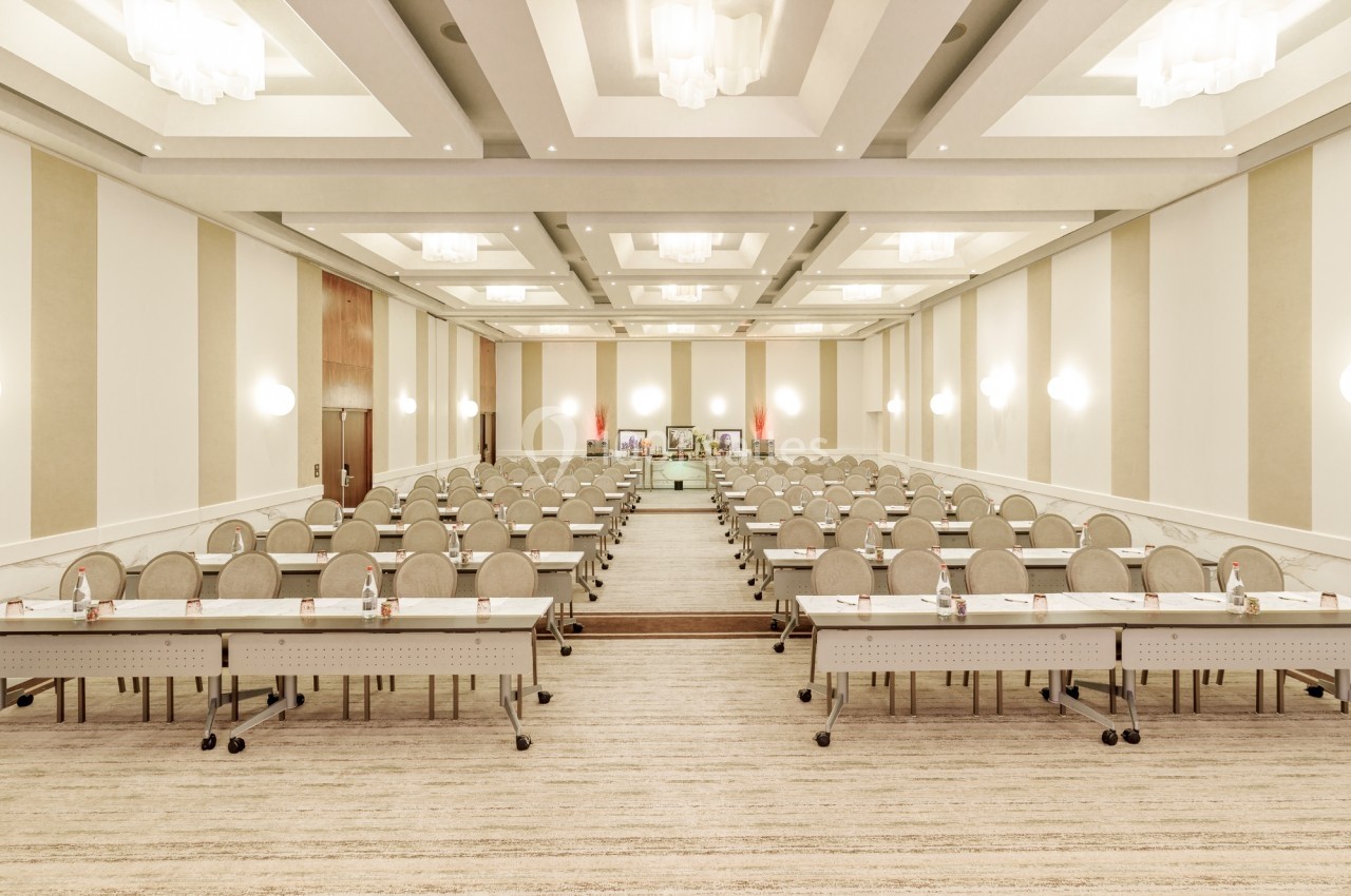Salle de conférence lumineuse avec rangées de tables et chaises alignées, prête pour une réunion ou un séminaire.