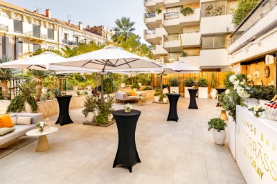 Transats avec coussins rouges alignés sur un ponton en bois, face à la mer, avec parasols blancs et vue sur un phare.