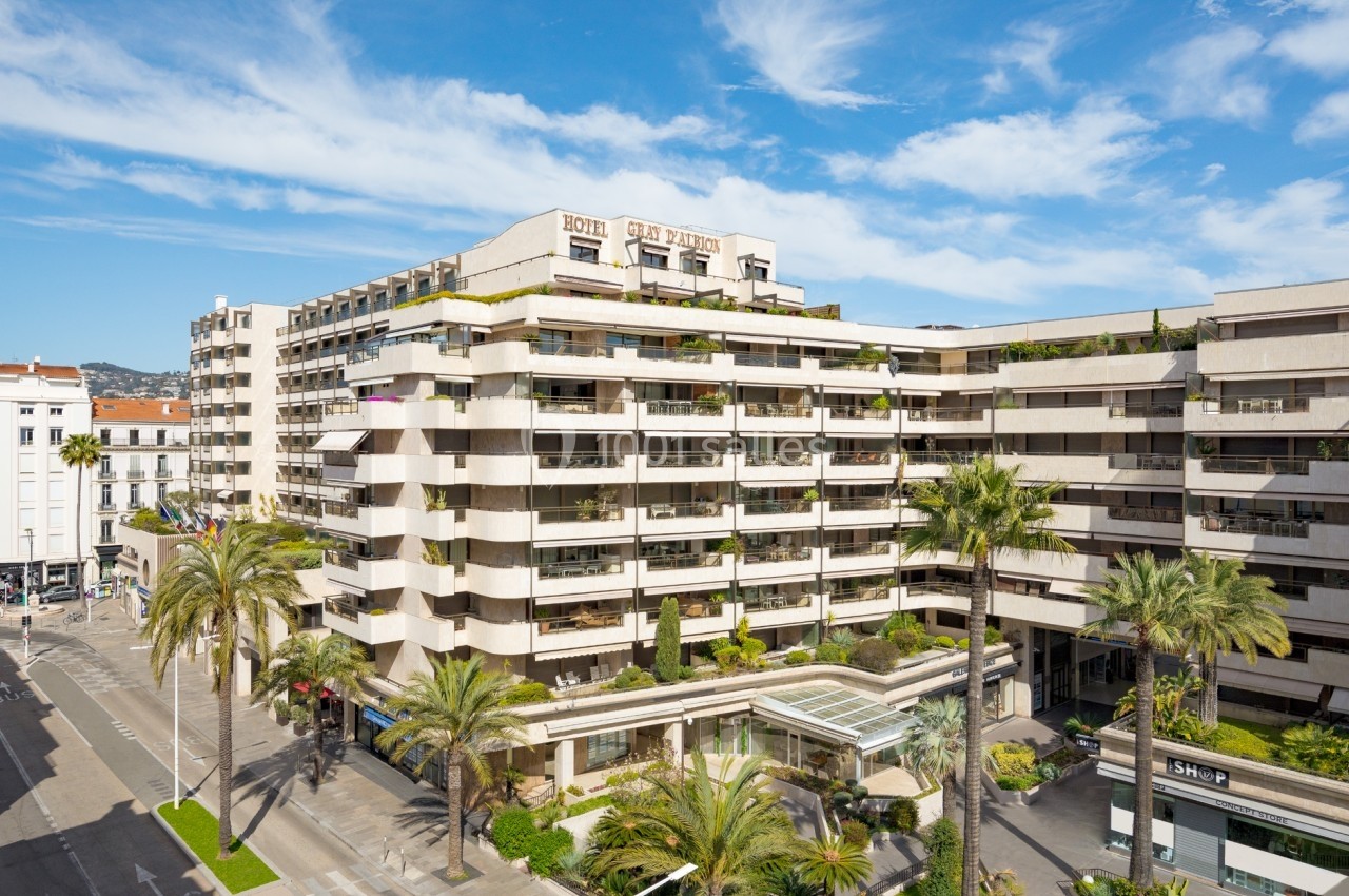 Façade d'un grand bâtiment moderne avec balcons, entouré de palmiers et situé à l'angle de deux rues.