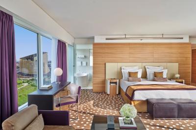 Chambre d'hôtel moderne avec grand lit, bureau, fauteuil, vue sur l'extérieur et salle de bain attenante.