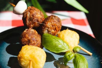 Brochettes avec boulettes de viande, fromage frit et feuille de basilic, servies sur une assiette bleue.