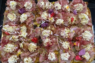 Plateau garni de charcuterie, fromages frais, fleurs comestibles et pousses, présenté sur un fond doré.