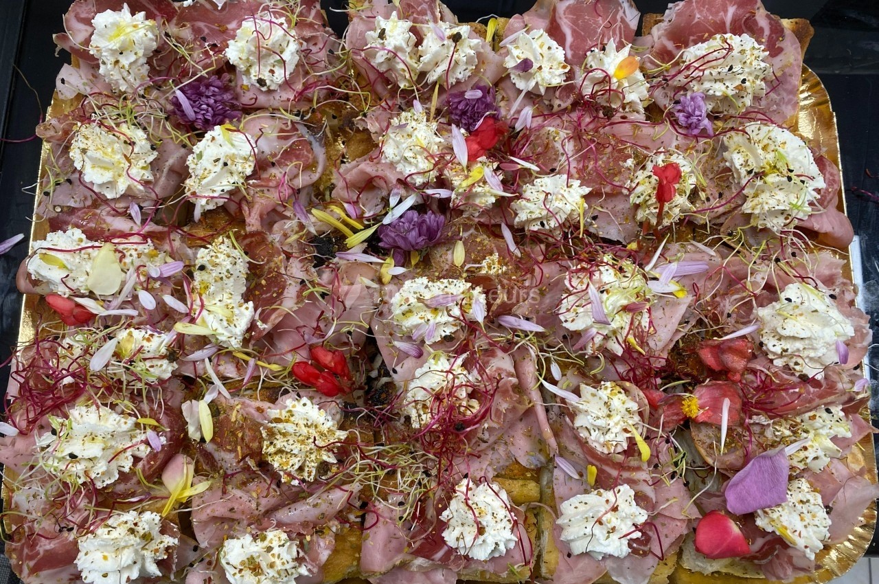 Plateau garni de charcuterie, fromages frais, fleurs comestibles et pousses, présenté sur un fond doré.