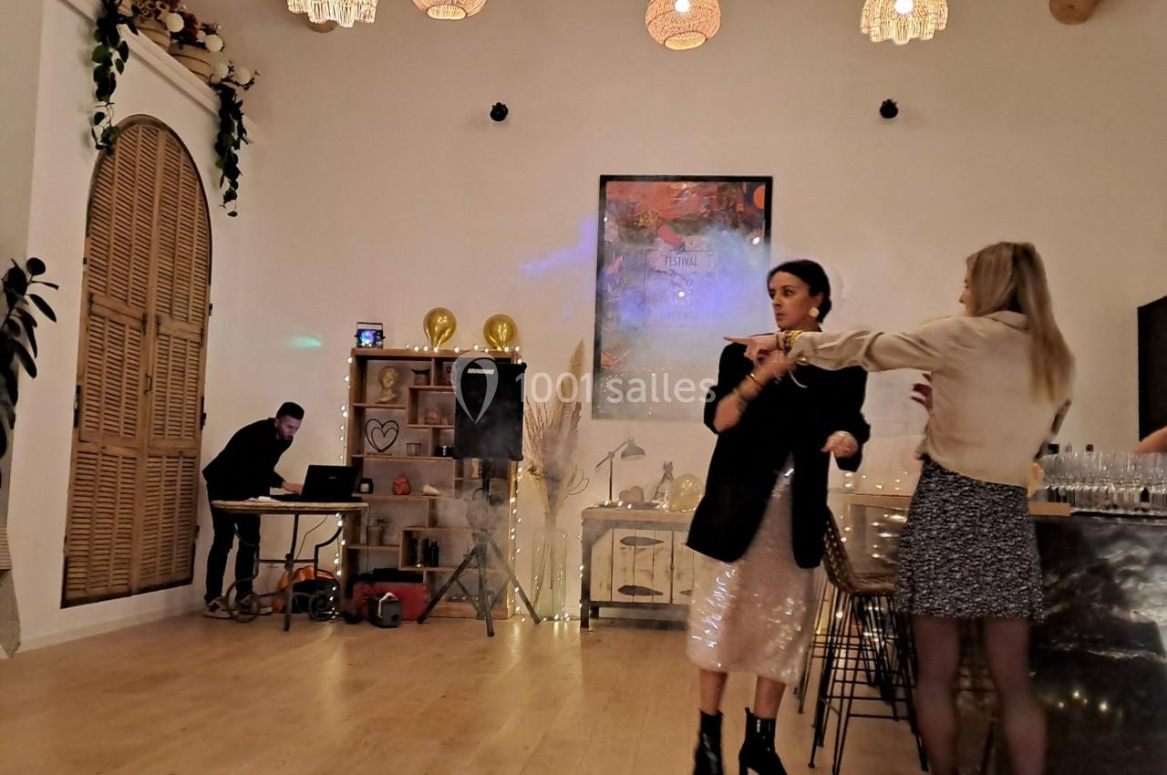 Deux femmes discutent près d'un bar dans une salle décorée, avec un DJ en arrière-plan.