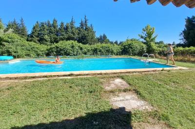 Maison avec terrasse entourée de végétation, située dans un jardin avec allée en gravier et ciel dégagé en arrière-plan.