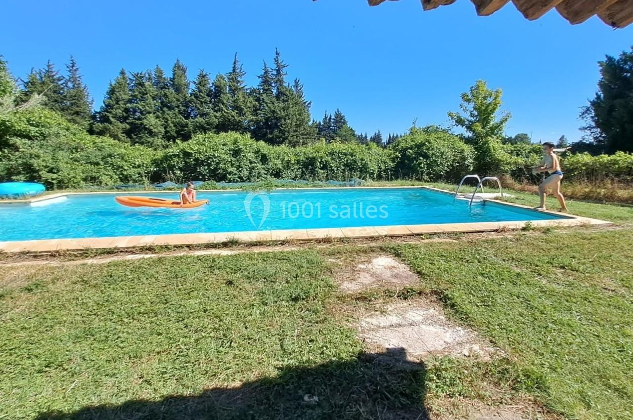 Une piscine extérieure entourée de verdure, avec une personne sur un matelas gonflable et une autre au bord.
