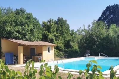 Maison avec terrasse entourée de végétation, située dans un jardin avec allée en gravier et ciel dégagé en arrière-plan.