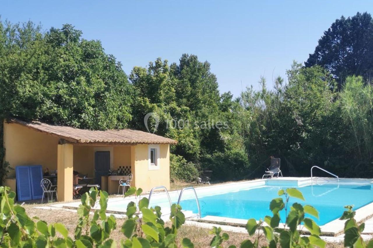 Piscine extérieure entourée de verdure avec un petit bâtiment jaune à toit en tuiles sur le côté.