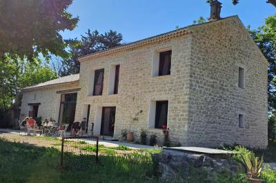 Maison avec terrasse entourée de végétation, située dans un jardin avec allée en gravier et ciel dégagé en arrière-plan.