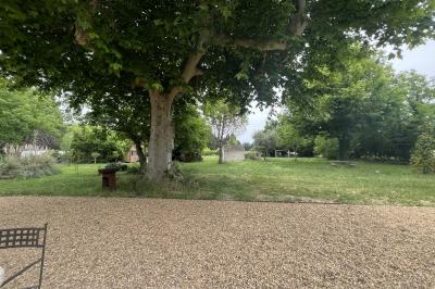 Maison avec terrasse entourée de végétation, située dans un jardin avec allée en gravier et ciel dégagé en arrière-plan.