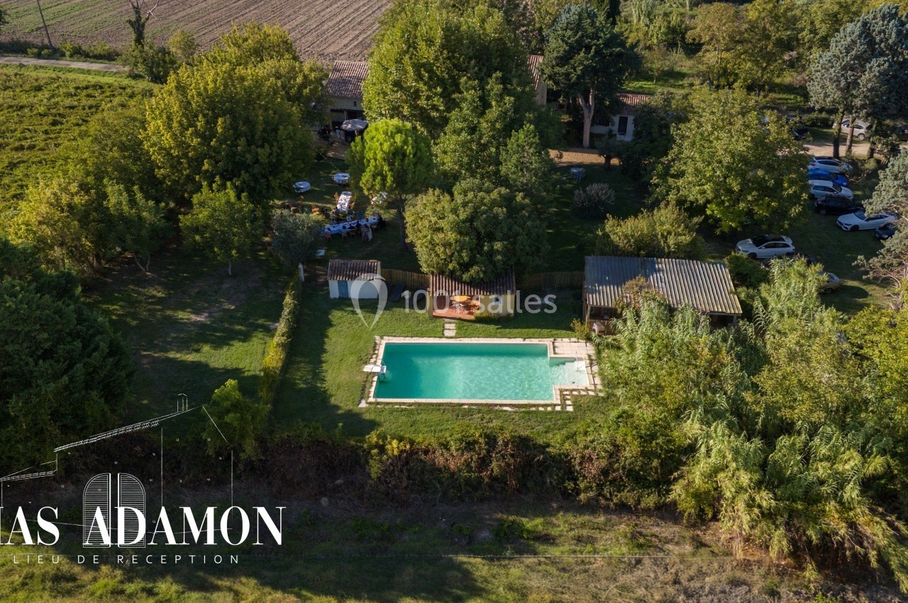 Vue aérienne d'un domaine avec piscine, espaces verts, bâtiments et véhicules stationnés en arrière-plan.