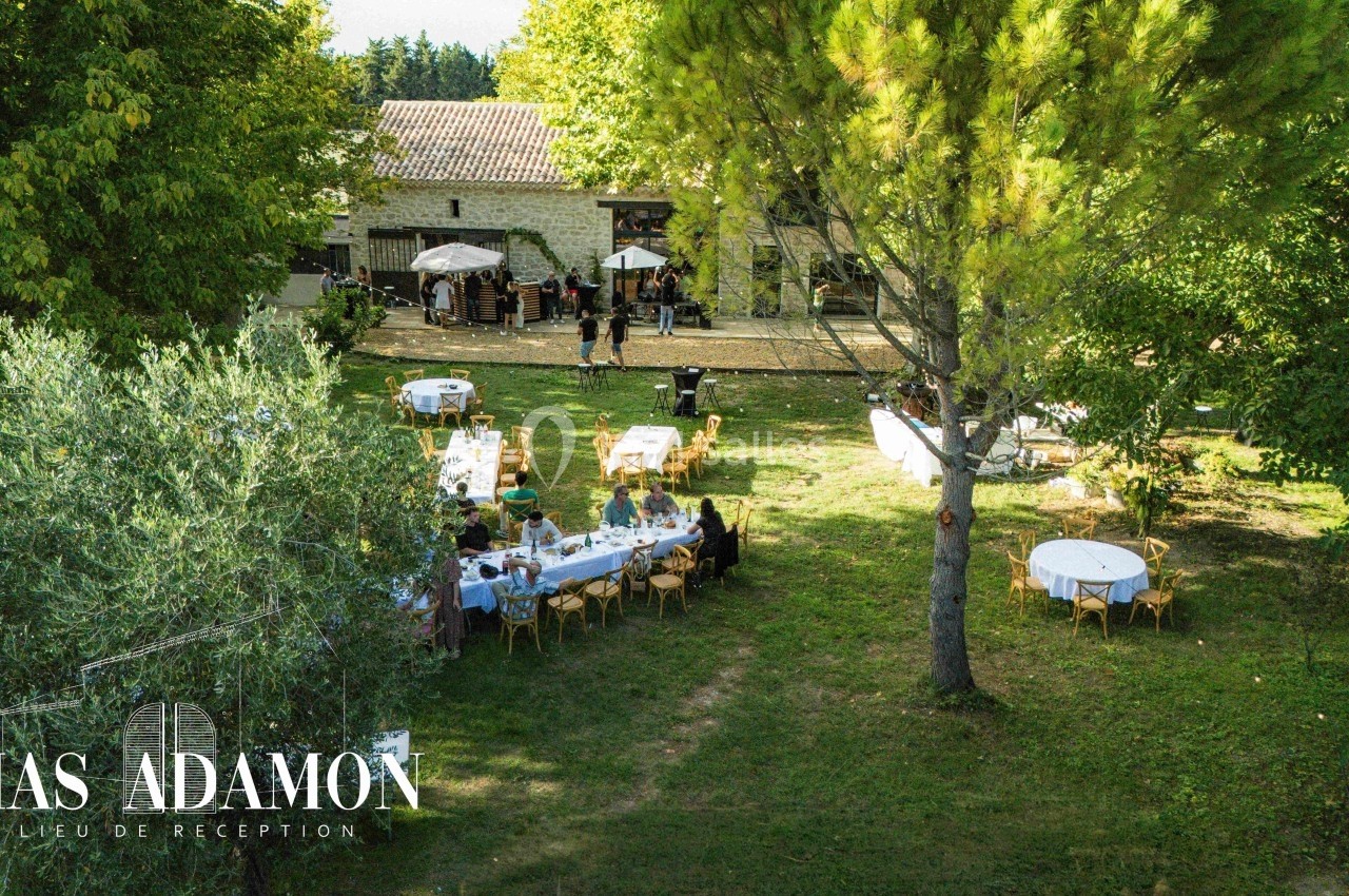 Vue aérienne d'un jardin avec des tables dressées pour un événement, entouré d'arbres et d'un bâtiment en pierre.