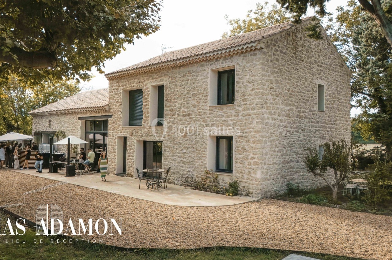 Bâtisse en pierre entourée de verdure avec une terrasse aménagée et des invités rassemblés à l'extérieur.