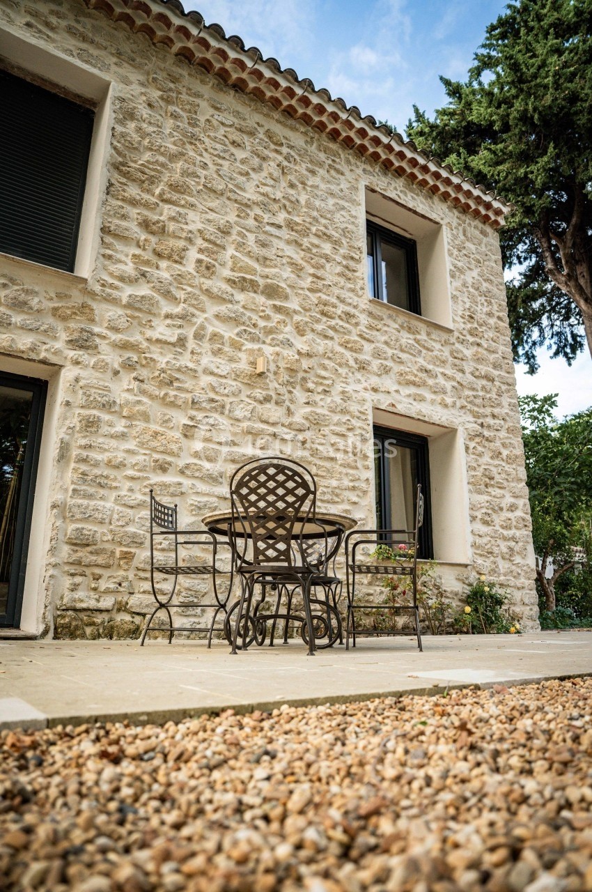 Façade en pierre d'une maison avec une terrasse aménagée, comprenant une table et des chaises en métal.