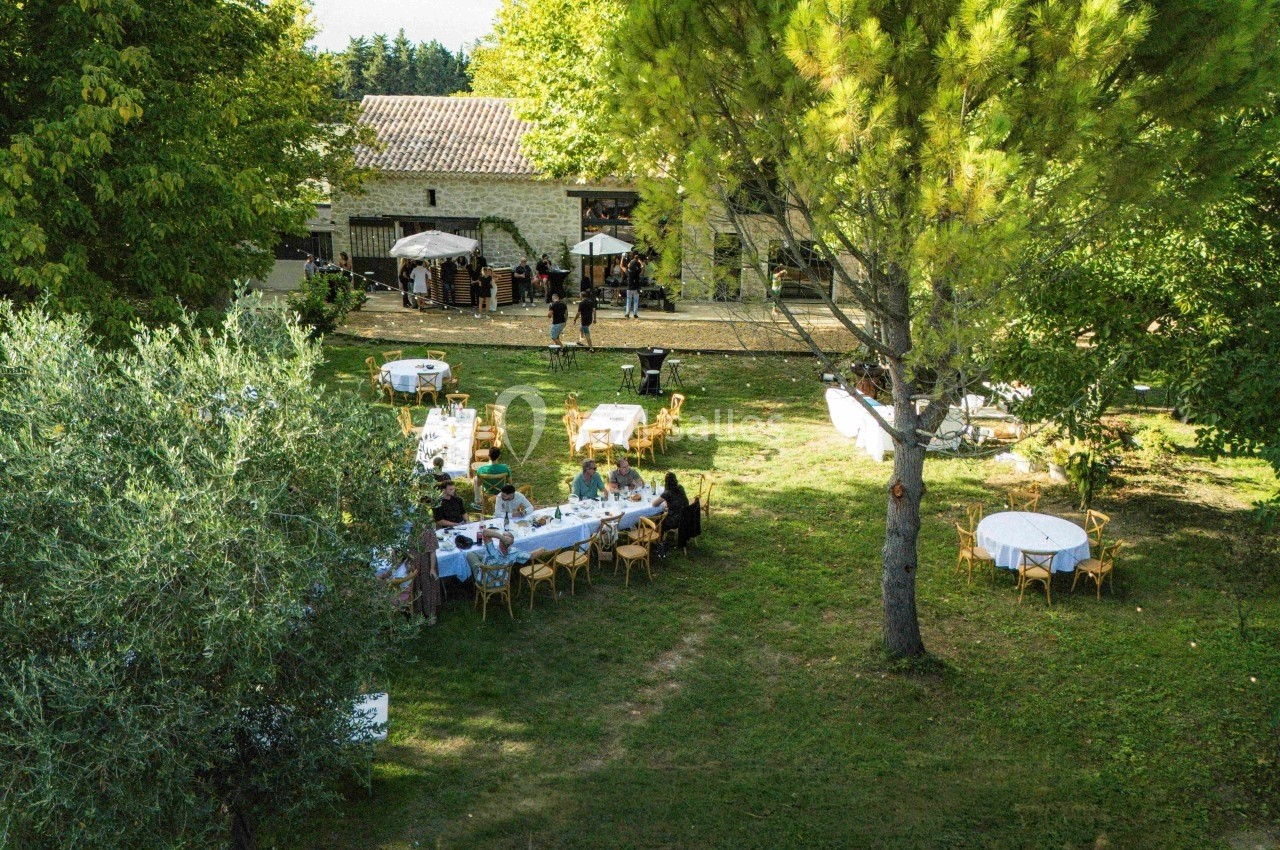 Vue aérienne d'un jardin avec des tables dressées pour un événement en plein air près d'un bâtiment en pierre.