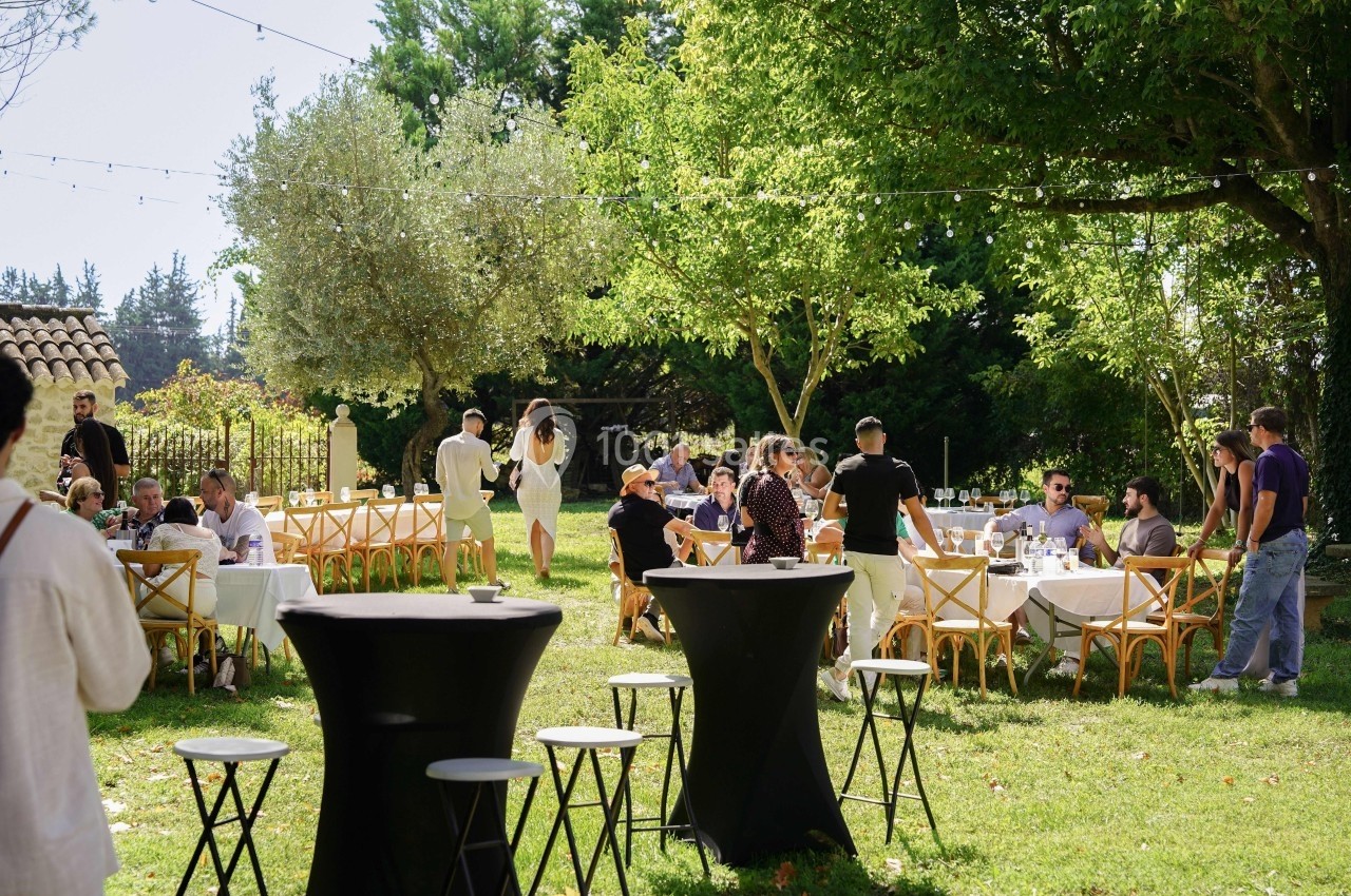 Groupe de personnes discutant et partageant un repas en plein air dans un jardin ombragé avec des tables dressées.