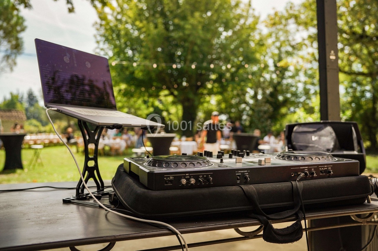 Table de mixage avec ordinateur portable posée sur une table en extérieur, dans un cadre verdoyant avec des invités en…