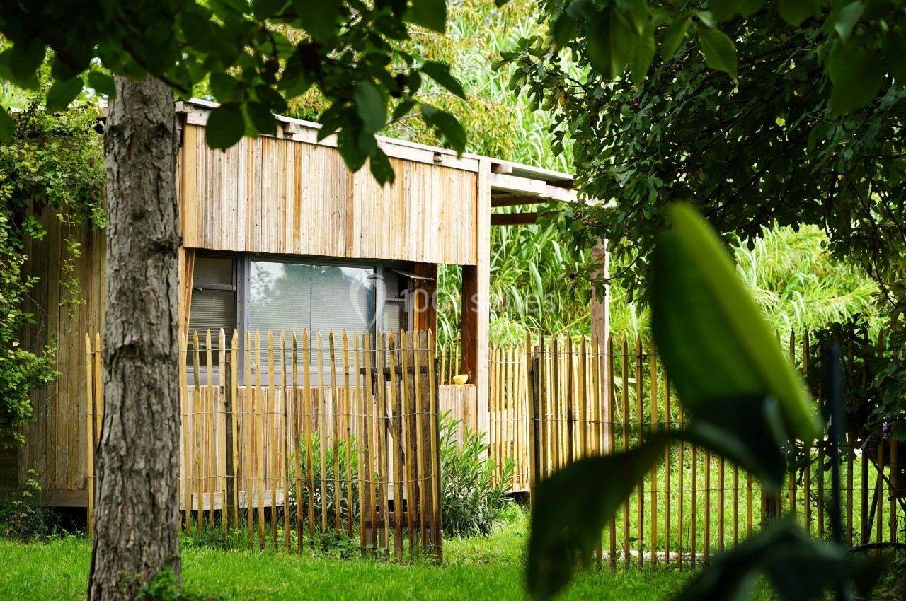 Cabane en bois entourée de végétation luxuriante et clôturée par des piquets en bambou.