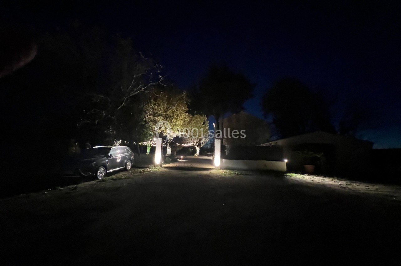 Allée sombre éclairée par des lampadaires, avec des arbres et une voiture garée sur le côté.