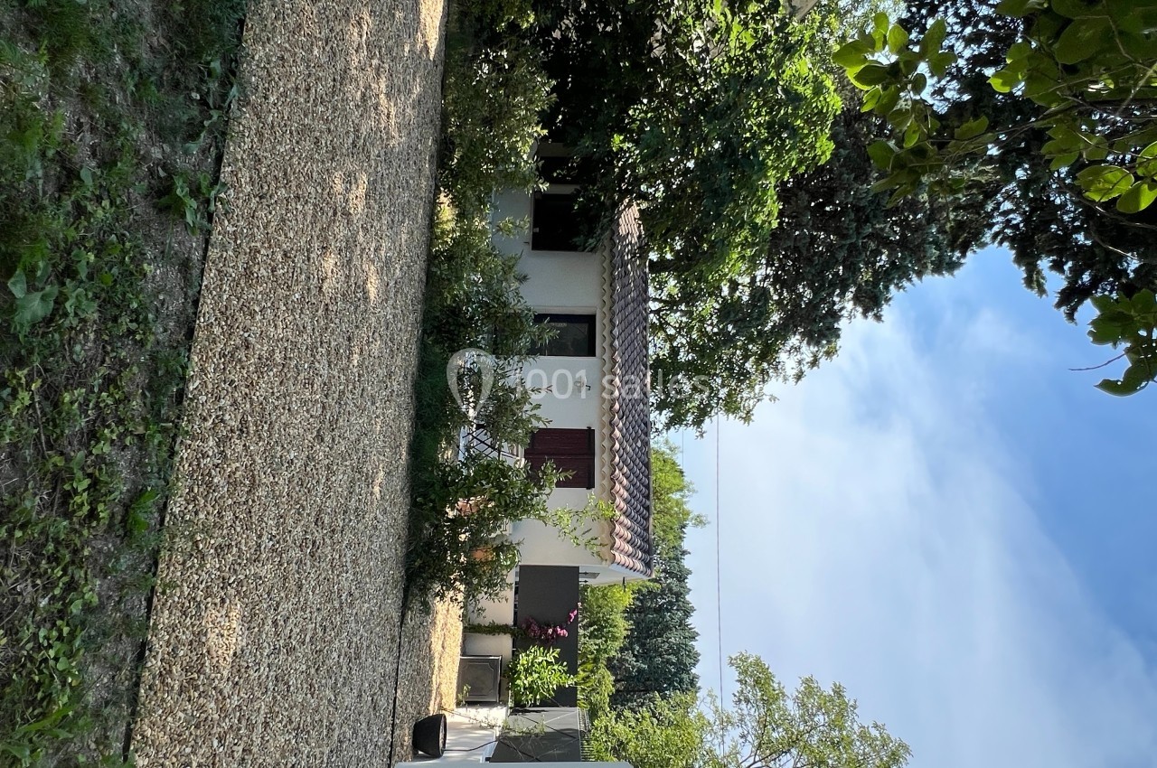 Maison blanche avec volets rouges entourée de végétation, allée en gravier au premier plan et ciel dégagé.
