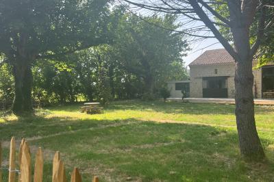 Maison avec terrasse entourée de végétation, située dans un jardin avec allée en gravier et ciel dégagé en arrière-plan.