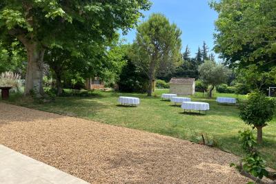 Maison avec terrasse entourée de végétation, située dans un jardin avec allée en gravier et ciel dégagé en arrière-plan.