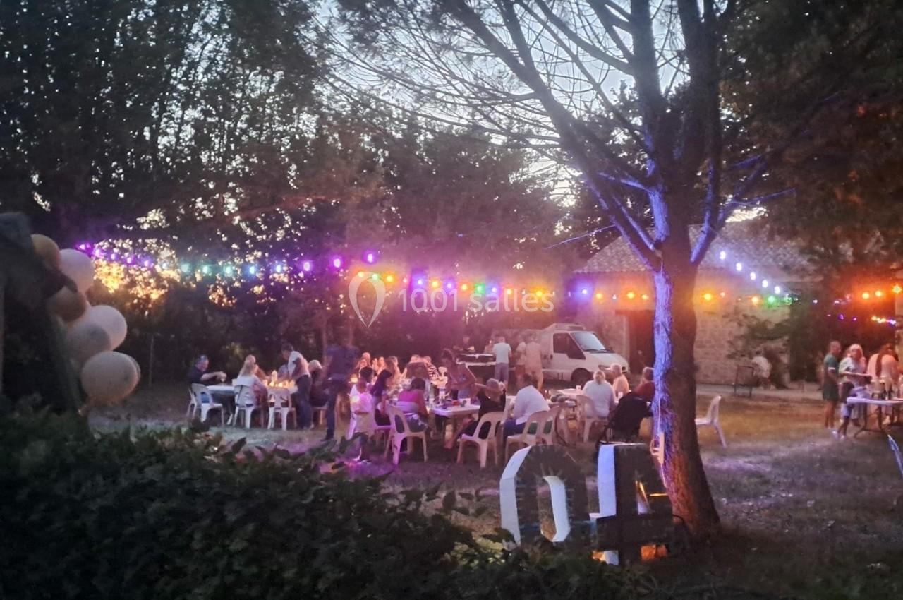 Des personnes dînent en plein air sous des guirlandes lumineuses colorées, entourées d'arbres au crépuscule.