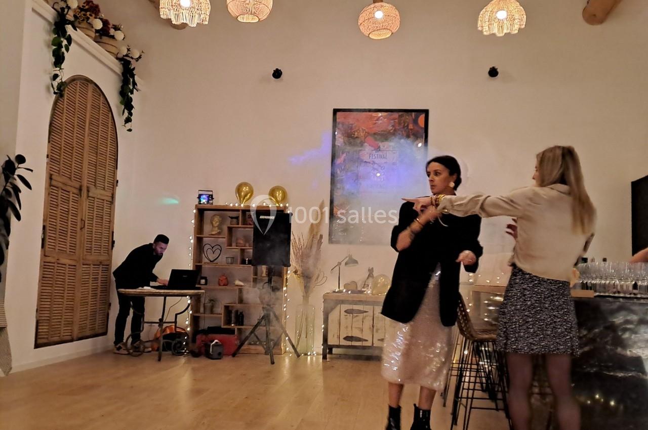 Deux femmes discutent dans une salle lumineuse avec un DJ en arrière-plan et une décoration chaleureuse.