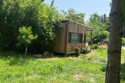 Maison avec terrasse entourée de végétation, située dans un jardin avec allée en gravier et ciel dégagé en arrière-plan.