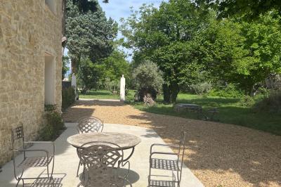 Maison avec terrasse entourée de végétation, située dans un jardin avec allée en gravier et ciel dégagé en arrière-plan.